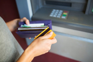 close up of hands with cash and credit card at atm machine